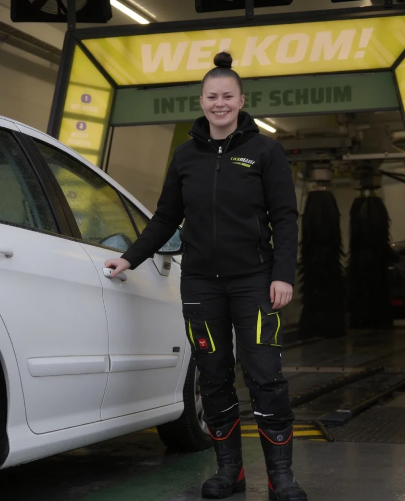 Een medewerker van Carwash Boxtel die naast een auto staat terwijl ze aan het lachten is.