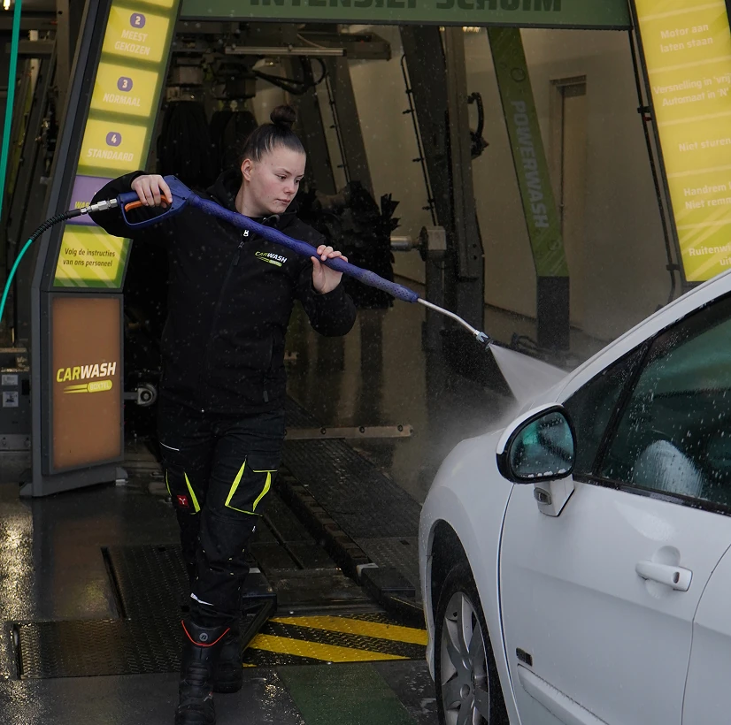 Vrouw die de een auto aan het voor spuiten is voor dat die de wasstraat in gaat.